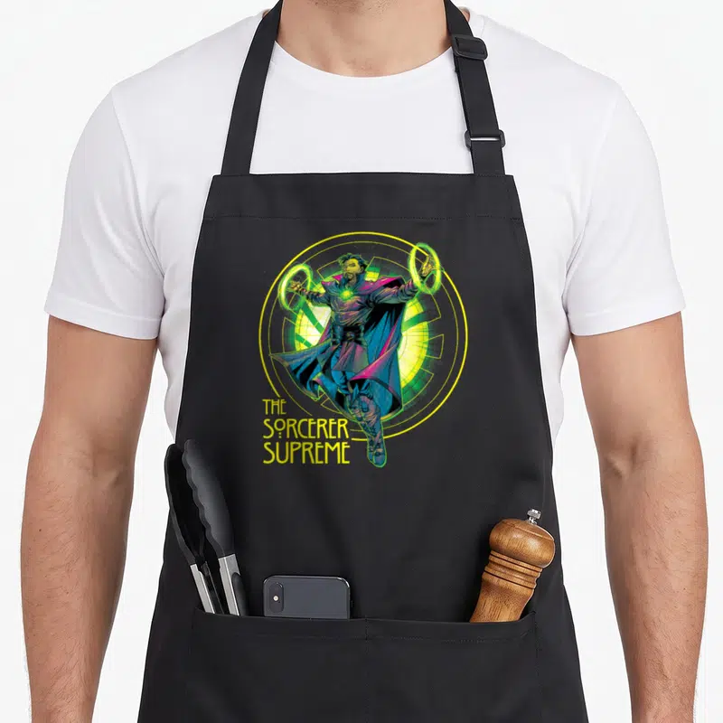 Tablier de cuisine noir avec illustration du Sorcier Suprême et anneaux magiques jaunes et verts.