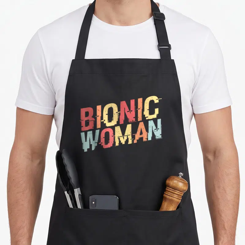 Tablier de cuisine noir avec inscription Bionic Woman en lettres colorées et effet dégradé vintage.
