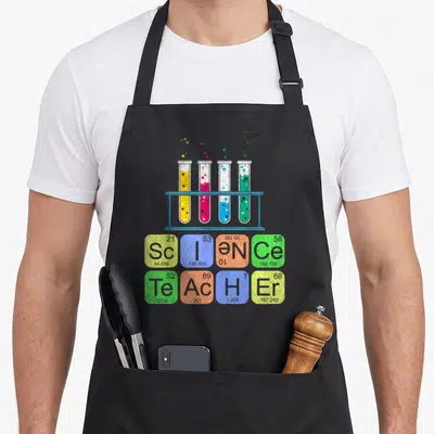 Tablier de cuisine noir avec quatre tubes à essais colorés sur support et éléments chimiques disposés en grille sous forme de message.