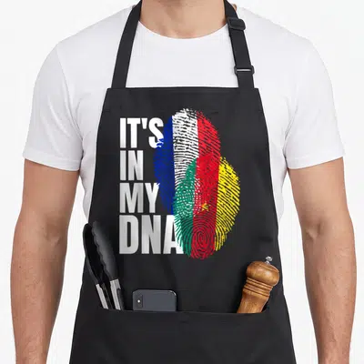 Tablier de cuisine noir avec inscription It's in my DNA et empreintes digitales aux couleurs des drapeaux français et camerounais.