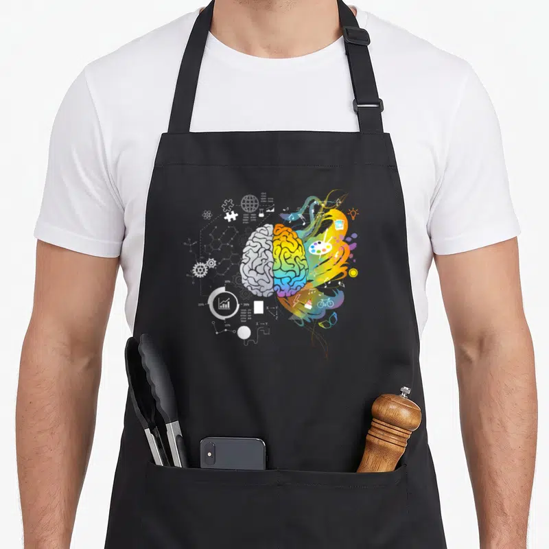 Tablier de cuisine noir avec illustration d'un cerveau coloré séparant logique scientifique et art créatif multicolore.