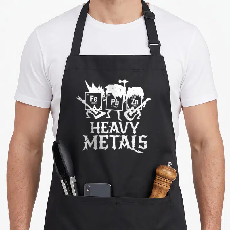 Tablier de cuisine noir avec trois éléments chimiques Fe Pb Zn jouant de la guitare sous le texte Heavy Metals en blanc.