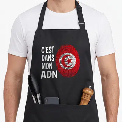 Tablier de cuisine noir avec une empreinte digitale rouge stylisée en drapeau tunisien et texte blanc vertical C'est dans mon ADN