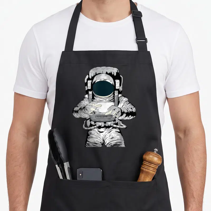 Tablier de cuisine noir avec illustration d'un astronaute en tenue spatiale blanche et noire.
