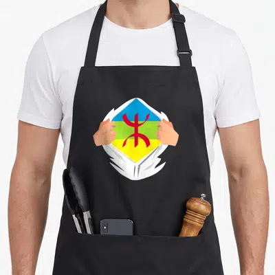 Tablier de cuisine noir avec illustration de mains déchirant un vêtement révélant le symbole Amazige aux couleurs vives.