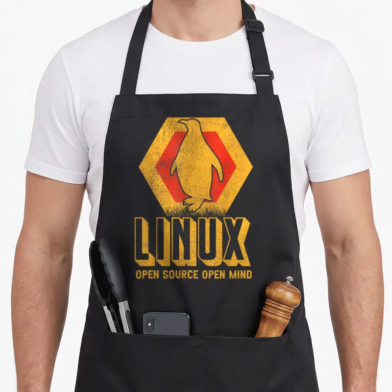 Tablier de cuisine noir avec un pingouin Linux stylisé dans un hexagone orange et rouge, le mot Linux en grandes lettres jaunes en dessous.