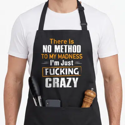 Tablier de cuisine noir avec inscription blanche et orange There Is No Method To My Madness I'm Just Fucking Crazy.