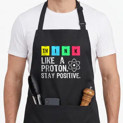 Tablier de cuisine noir avec les mots THINK en cases colorées et le texte Like A Proton Stay Positive en blanc.