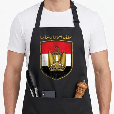 Tablier de cuisine noir avec blason égyptien vintage, aigle doré et texte en arabe sur fond tricolore rouge blanc noir.