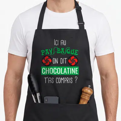 Tablier de cuisine noir avec le texte Ici au Pays-Basque on dit Chocolatine t'as compris et deux symboles rouges.