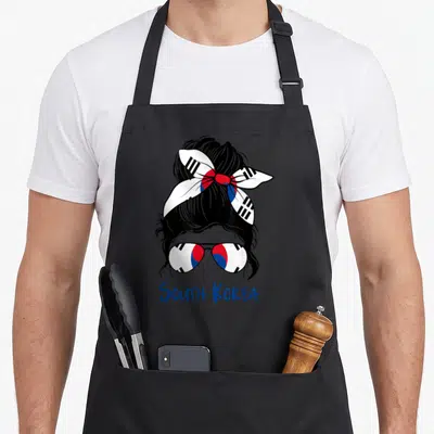 Tablier de cuisine noir avec une illustration de femme au chignon portant un bandana et des lunettes aux motifs du drapeau sud-coréen.