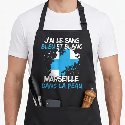 Tablier de cuisine noir avec drapeau bleu et blanc et texte J'ai le sang bleu et blanc Marseille dans la peau imprimé en centre.
