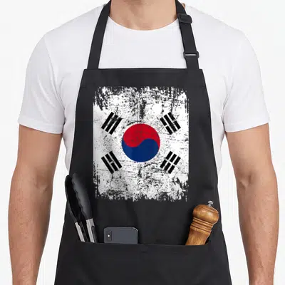 Tablier de cuisine noir avec le drapeau de la Corée du Sud dans un style grunge et délavé, centré sur le taegeuk rouge et bleu.