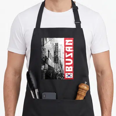 Tablier de cuisine noir avec illustration urbaine de Busan, bande rouge verticalet drapeau sud-coréen en bas à droite.