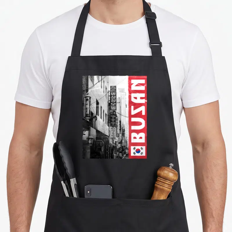 Tablier de cuisine noir avec illustration urbaine de Busan, bande rouge verticalet drapeau sud-coréen en bas à droite.