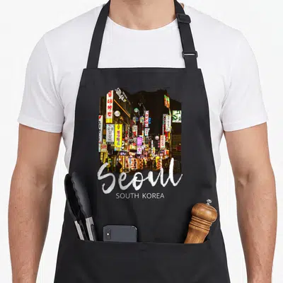 Tablier de cuisine noir avec une illustration de rues animées à Séoul et l'inscription Seoul South Korea en blanc.