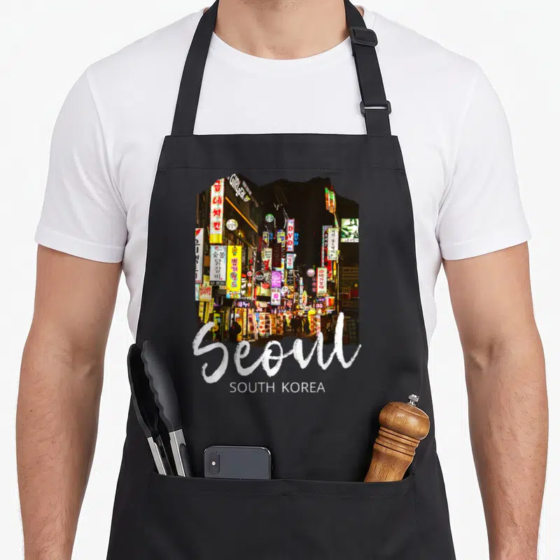 Tablier de cuisine noir avec une illustration de rues animées à Séoul et l'inscription Seoul South Korea en blanc.