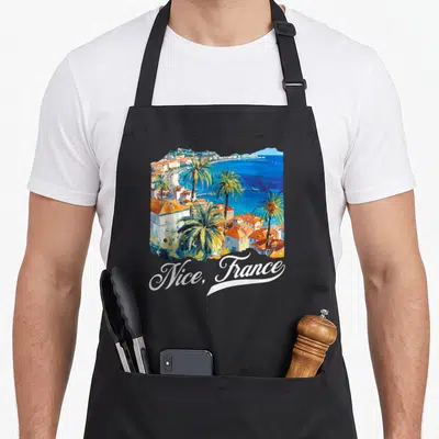Tablier de cuisine noir avec illustration colorée de Nice, France et palmiers au bord de la mer.