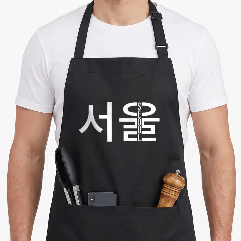 Tablier de cuisine noir avec inscription Seoul en lettres latines verticales intégrées aux caractères d'écriture Hangul blancs.