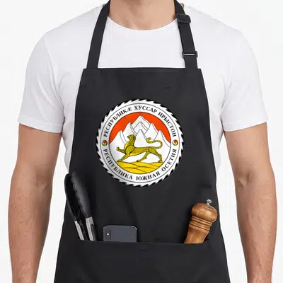 Tablier de cuisine noir avec l'emblème circulaire de l'Ossétie du Sud montrant un léopard et des montagnes.