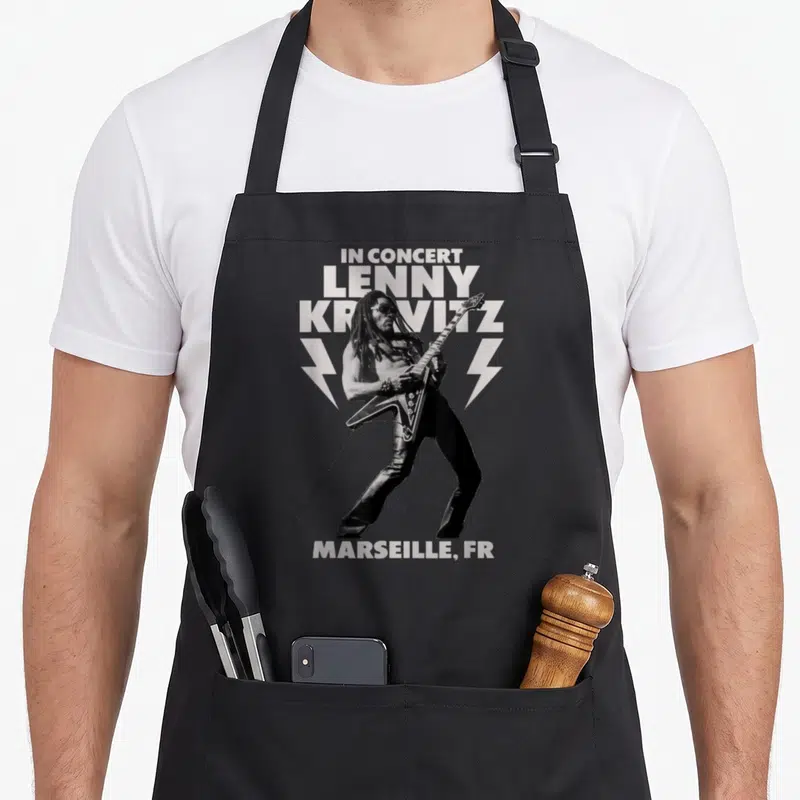 Tablier de cuisine noir avec illustration monochrome d'un musicien jouant de la guitare et le texte In Concert Lenny Kravitz Marseille FR.