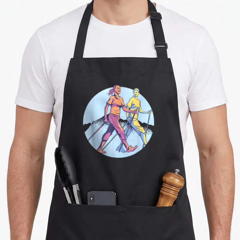 Tablier de cuisine noir avec une illustration colorée de deux femmes pratiquant la marche nordique dans un décor montagneux.
