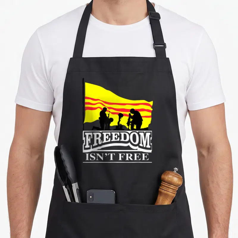 Tablier de cuisine noir avec drapeau Vietnam du Sud jaune et rouge, silhouettes militaires et texte Freedom Isn't Free en blanc.
