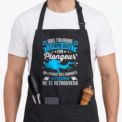 Tablier de cuisine noir avec silhouette bleue de plongeur et texte blanc souligné par des coquillages et étoiles.