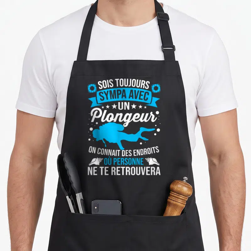Tablier de cuisine noir avec silhouette bleue de plongeur et texte blanc souligné par des coquillages et étoiles.