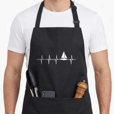 Tablier de cuisine noir avec une ligne de battement de cœur blanche intégrant un voilier au centre du design.