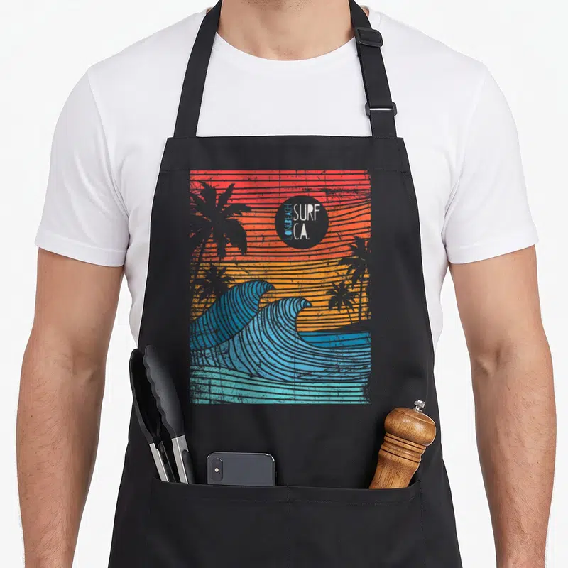 Tablier de cuisine noir avec vagues bleues, palmiers gris et logo Surf CA Long Beach sur fond orange rayé.