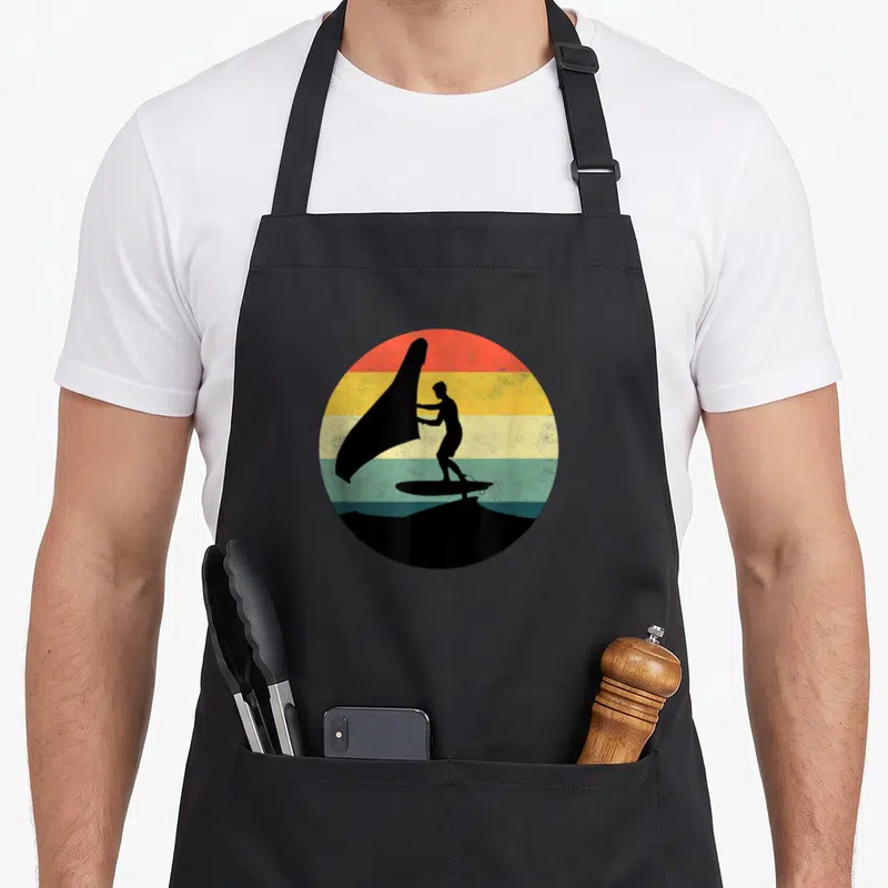 Tablier de cuisine noir avec silhouette d'un wingfoiler tenant une aile sur fond de bandes colorées rondes.