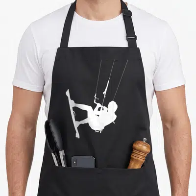 Tablier de cuisine noir avec une illustration blanche représentant un kitesurfeur suspendu par ses cordes au-dessus d'une planche.