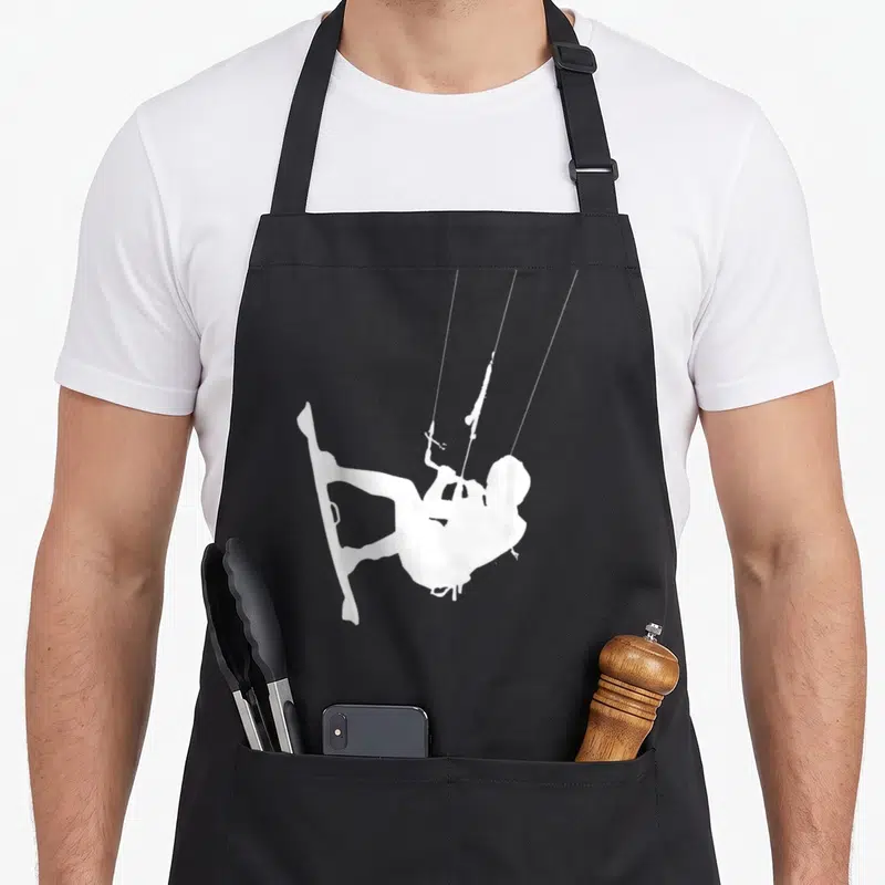 Tablier de cuisine noir avec une illustration blanche représentant un kitesurfeur suspendu par ses cordes au-dessus d'une planche.