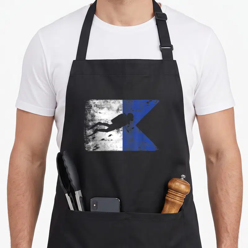 Tablier de cuisine noir avec un drapeau de plongée Alpha blanc et bleu comportant une silhouette de plongeur en apnée.