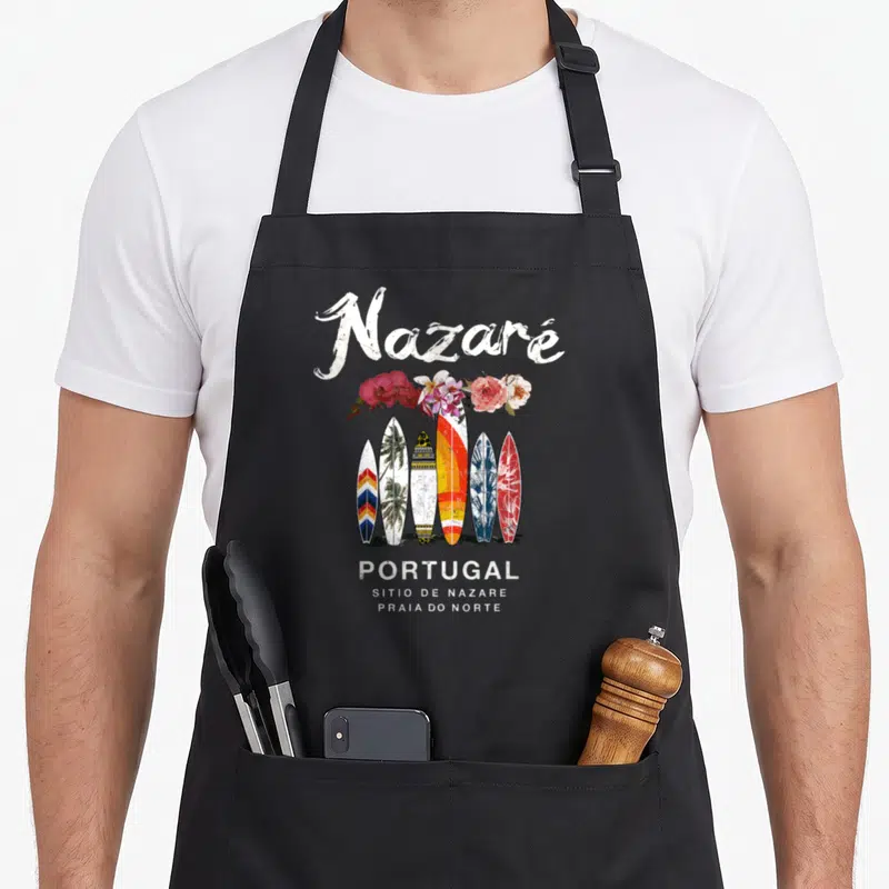 Tablier de cuisine noir avec six planches de surf colorées, fleurs roses et texte blanc Nazare Portugal en style vintage.
