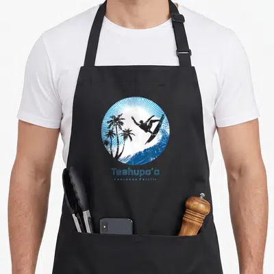 Tablier de cuisine noir avec illustration circulaire d'un surfeur, palmiers et le texte Teahupo'o Lagon Pacifique en bleu.