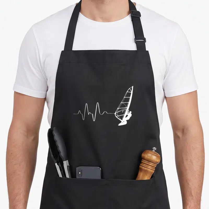 Tablier de cuisine noir avec illustration blanche d'un battement de cœur se terminant par un voilier de windsurf et une planche.