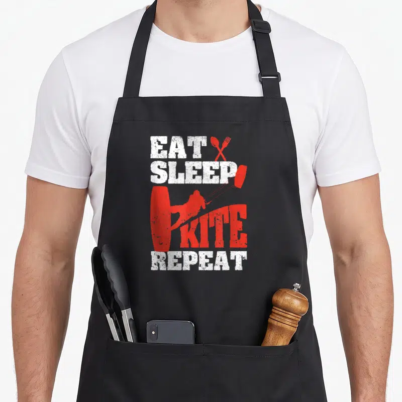 Tablier de cuisine noir avec illustration rouge d'un kitesurfeur et texte blanc Eat Sleep Kite Repeat.