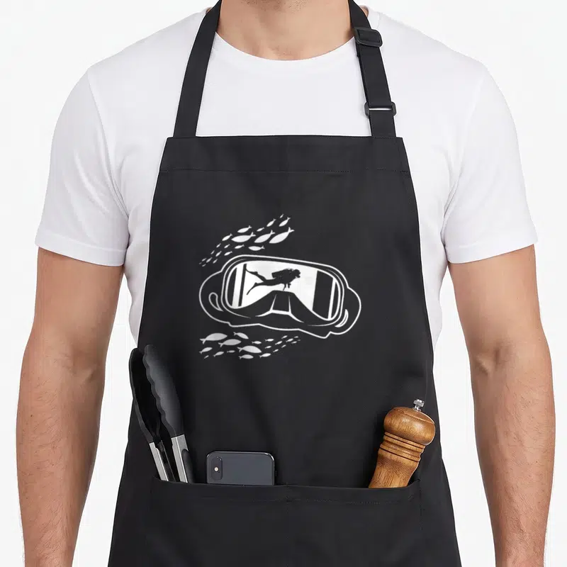 Tablier de cuisine noir avec masque de plongée blanc, silhouettes de plongeur et bancs de poissons stylisés.