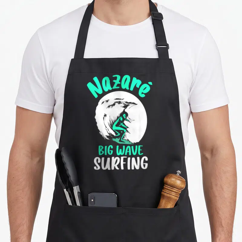 Tablier de cuisine noir avec illustration d'un surfeur sur une grande vague et le texte Nazaré Big Wave Surfing en vert et blanc.