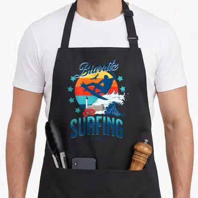 Tablier de cuisine noir avec illustration Biarritz Surfing Côte Basque et silhouettes de vagues.