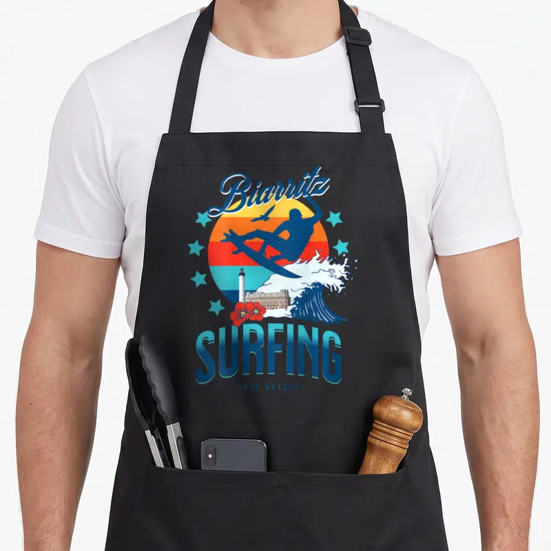 Tablier de cuisine noir avec illustration Biarritz Surfing Côte Basque et silhouettes de vagues.