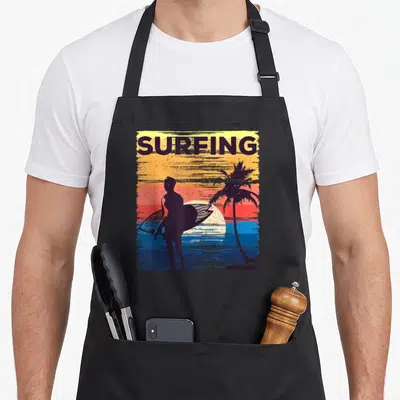 Tablier de cuisine noir avec silhouette surfeur planche de surf et palmier sur fond de coucher de soleil coloré vintage.