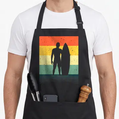 Tablier de cuisine noir avec silhouette d'homme tenant une planche de surf sur fond de bandes colorées vintage.