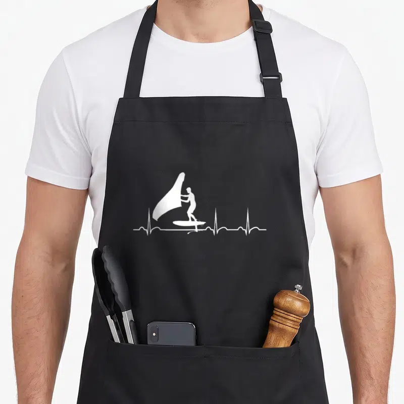 Tablier de cuisine noir avec silhouette blanche d'un wingfoiler sur une ligne de battement de cœur.