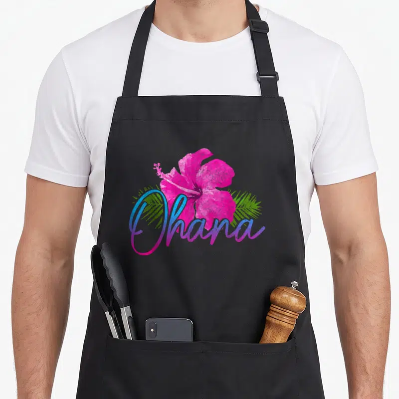 Tablier de cuisine noir avec hibiscus rose et texte Ohana coloré au centre