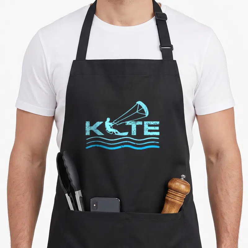 Tablier de cuisine noir avec logo KITE bleu clair représentant un kitesurfeur et des vagues stylisées en bas.