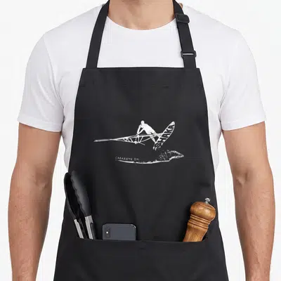 Tablier de cuisine noir avec illustration blanche d'un windsurfer effectuant un saut au-dessus d'une vague, inscriptions Shaka et Cabarete DR visibles.