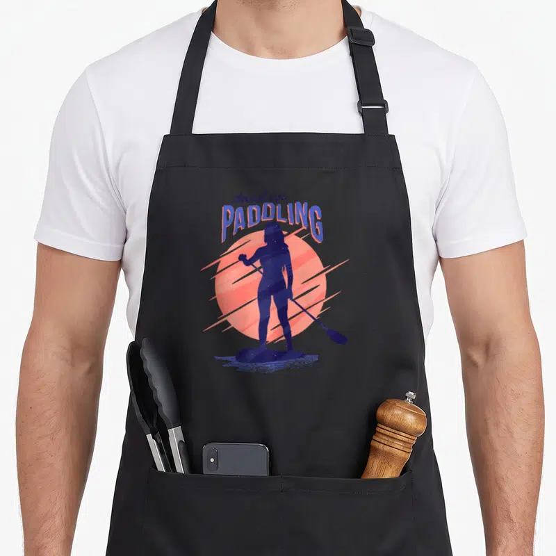 Tablier de cuisine noir avec silhouette de paddleuse, soleil rose et texte stand up PADDLING en bleu.
